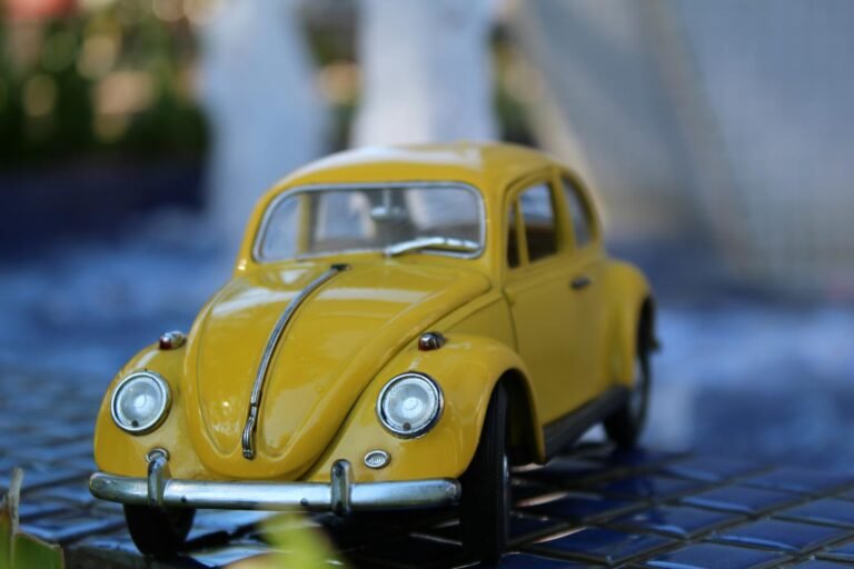 Close-up of a vintage yellow Volkswagen Beetle model toy car on a blue tile background.